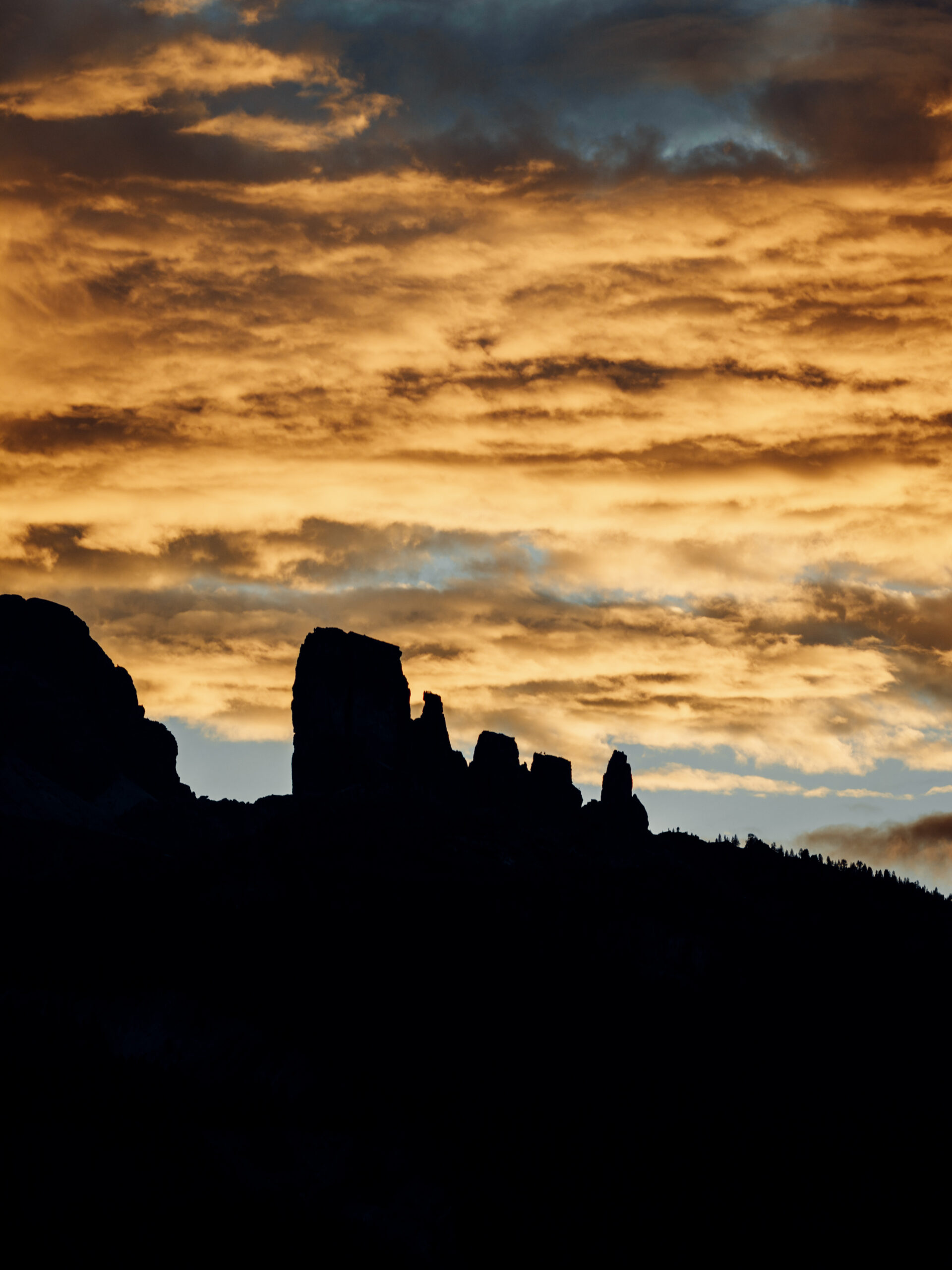 Silhouette of a rugged mountain ridge beneath a dramatic sky filled with warm orange and cool blue clouds at sunset—a perfect scene for any Travel Filmmaker, highlighting the peaks’ striking contrast against the colourful sky.
