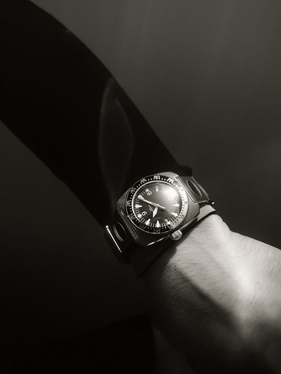 A close-up, black and white photo of a wrist wearing an analogue wristwatch with a dark strap, showing the time as approximately 10:12—capturing the timeless style of an Italian Content Creator. Soft light and shadows highlight the hand and watch.