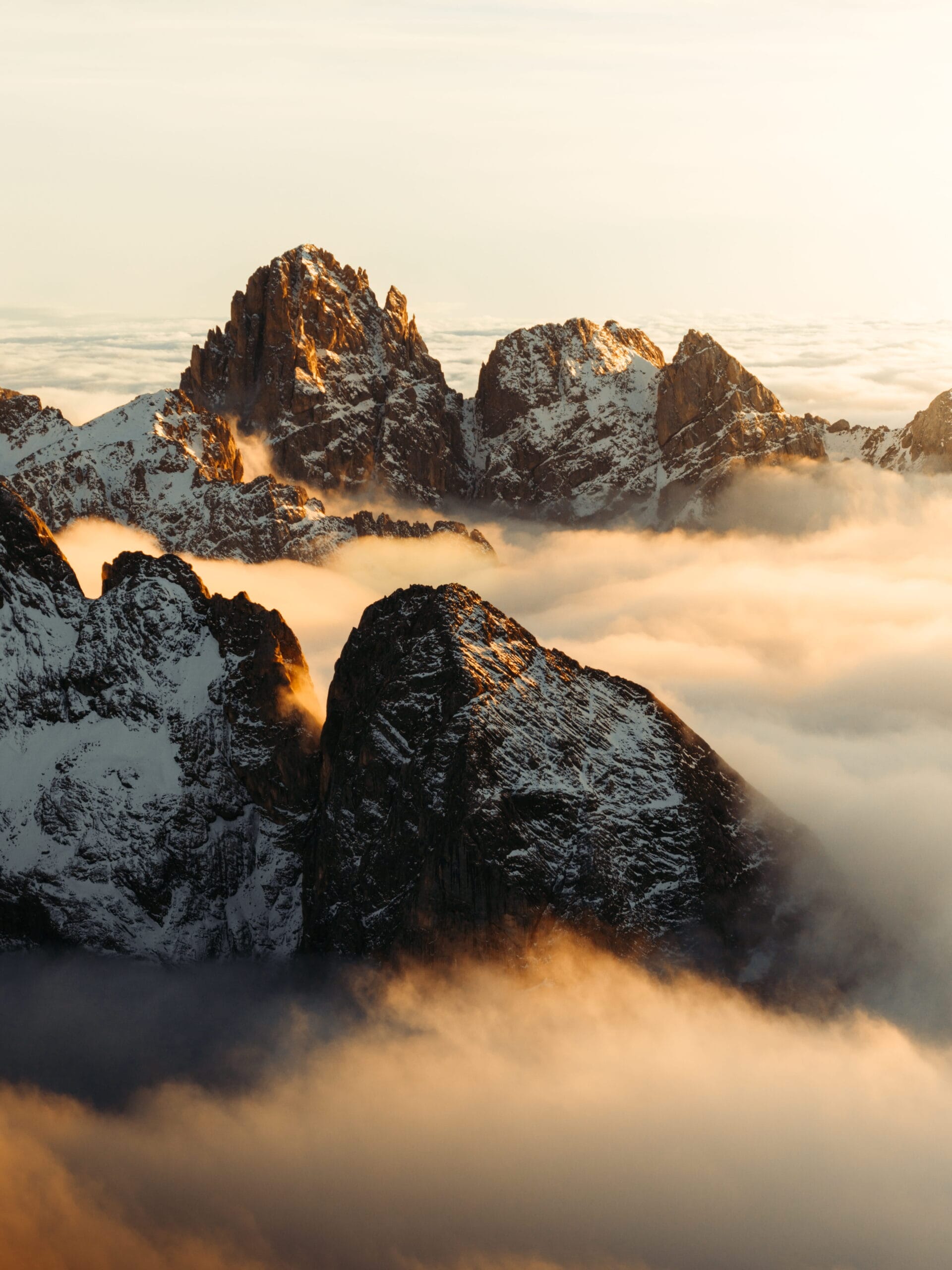 Sunlit mountain peaks rise above a sea of clouds, with snow covering rugged rocks and warm golden light illuminating the scene, creating a dramatic and serene landscape perfect for adventurous brands seeking inspiration.